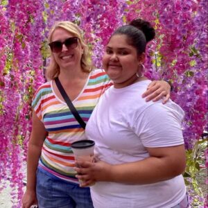 Two women standing in front of pink flowers.